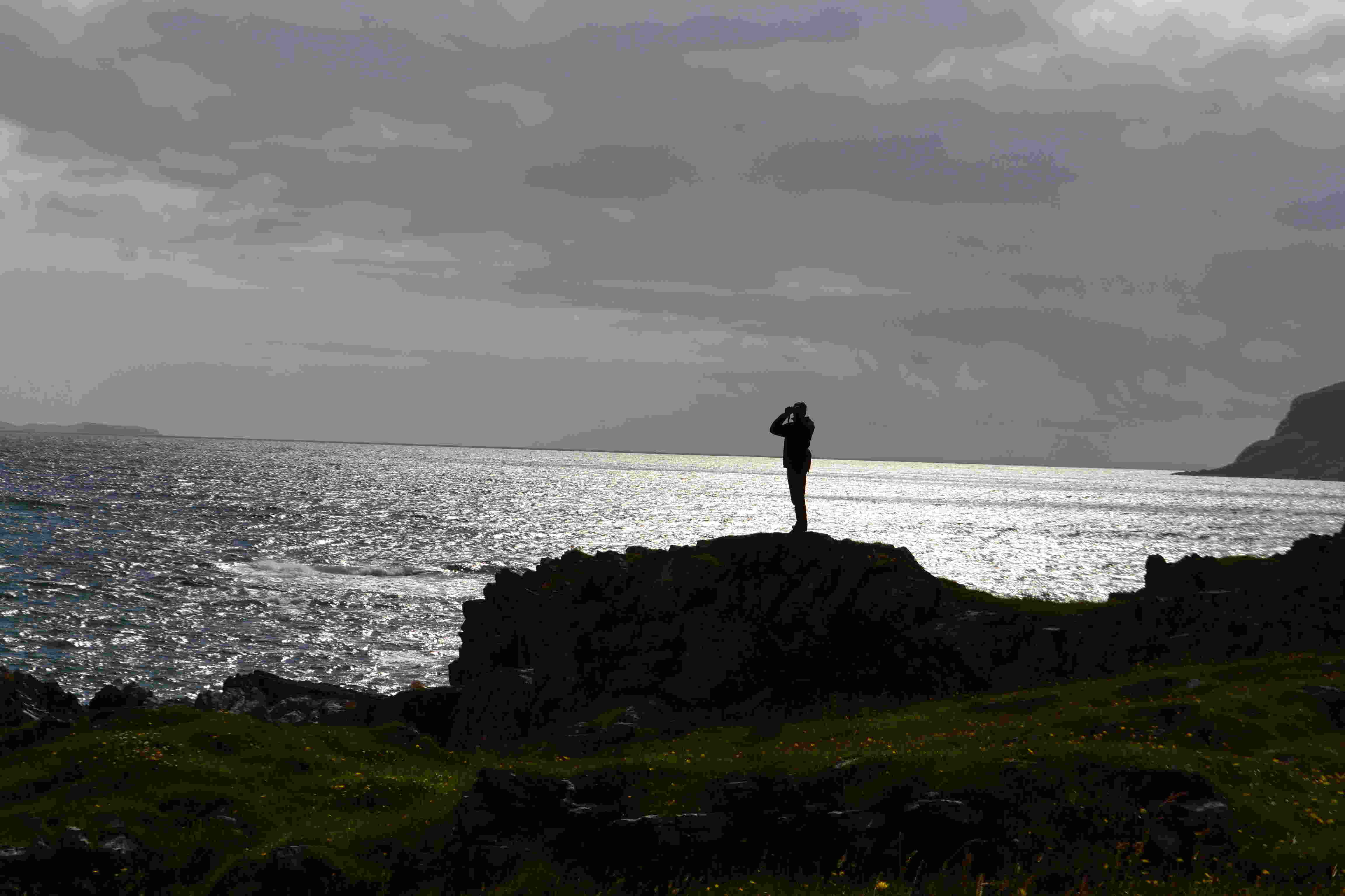 Silhouette d’une personne debout sur un rocher, face à la mer scintillante à contre-jour