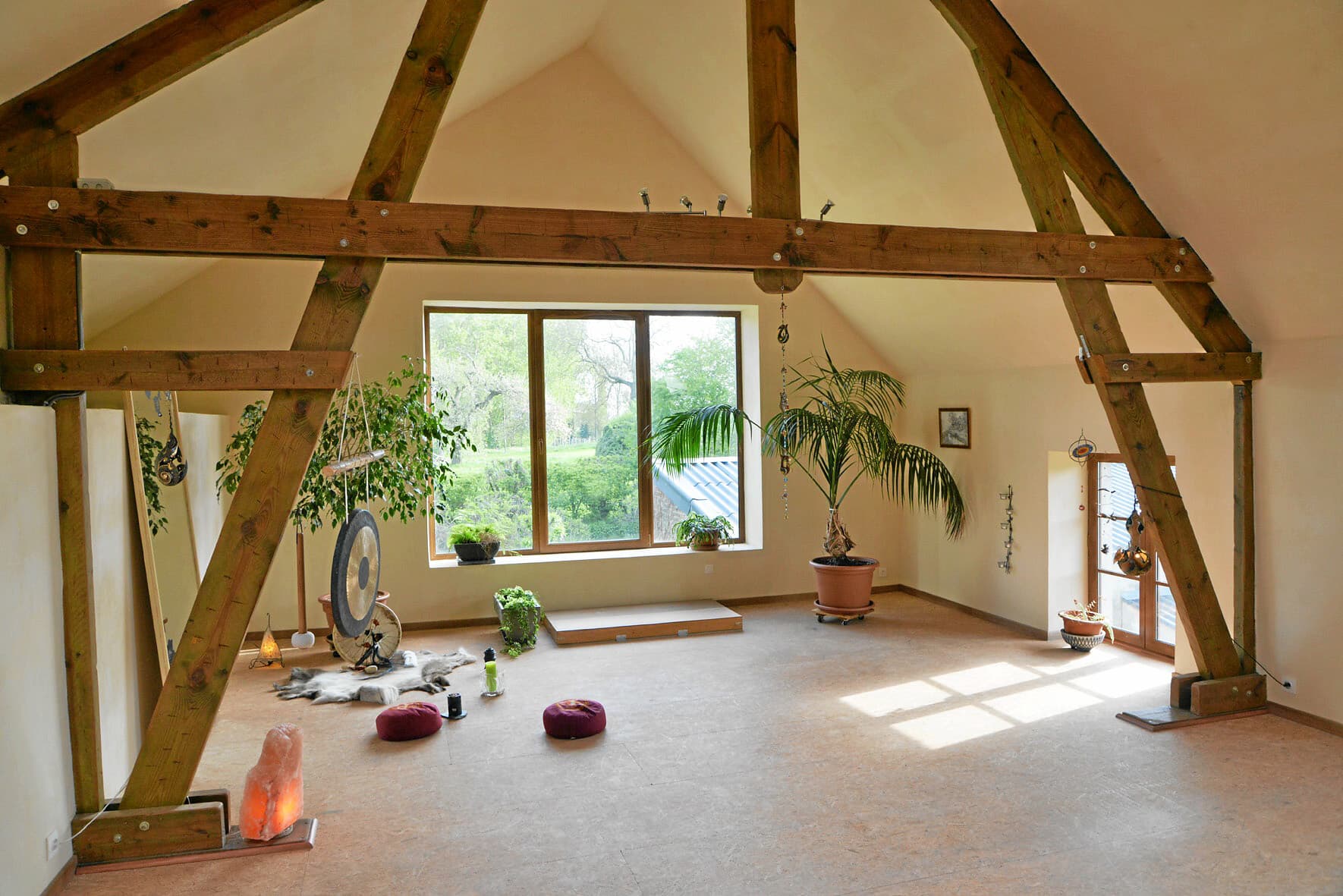 La salle de pratique de Montenaken sous sa charpente en bois : gong, coussins de méditation, plantes et lampe de sel