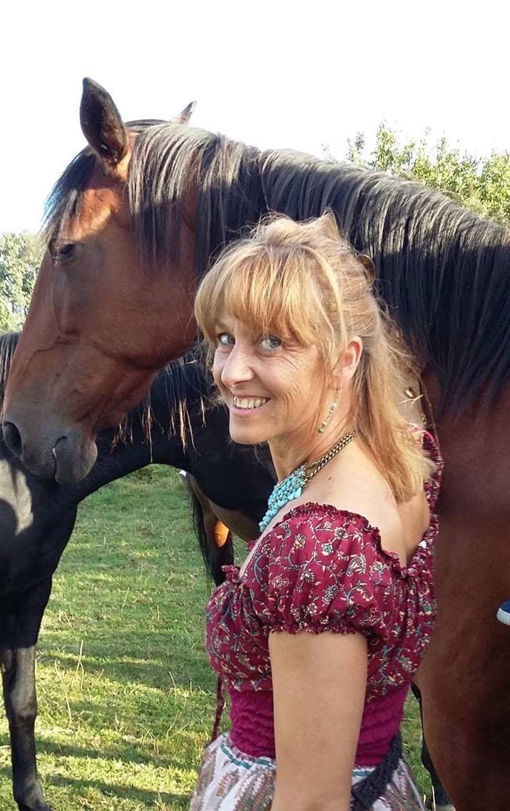 Véronique Linclau souriante aux côtés d’un cheval bai, dans un pré