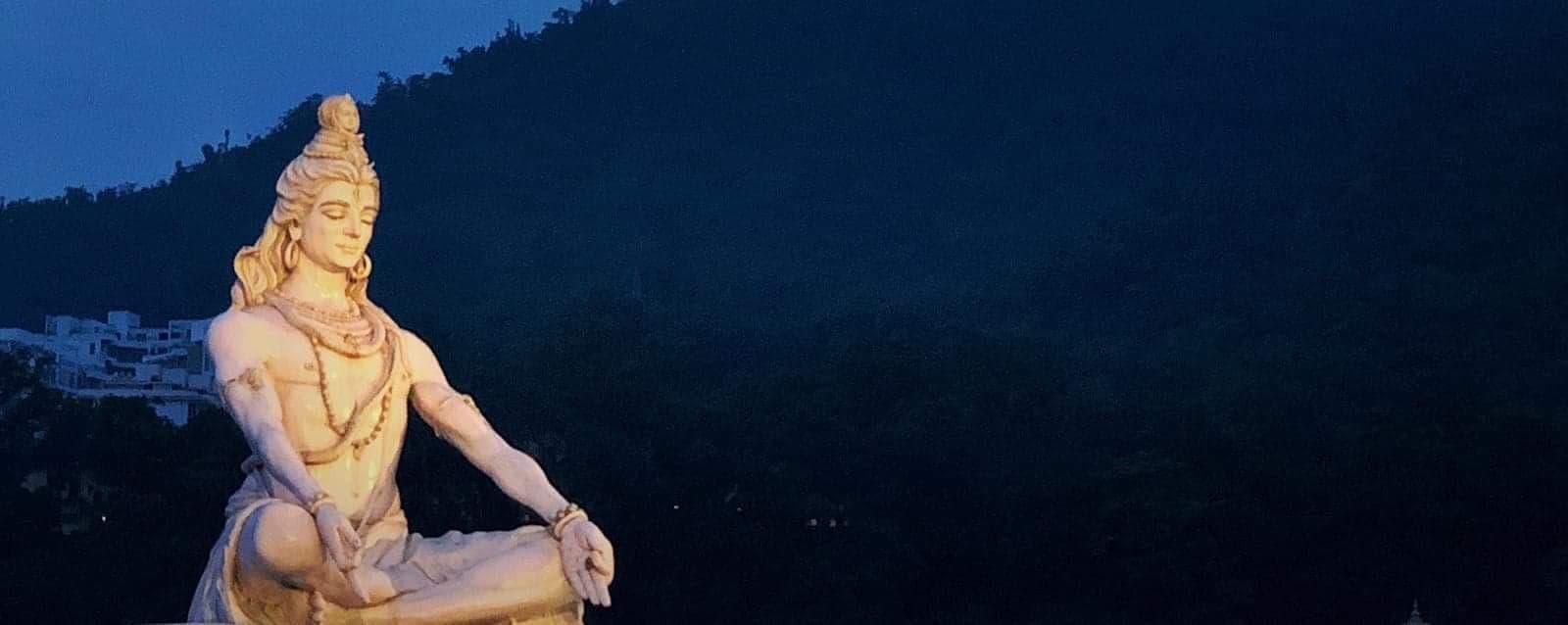 Statue blanche de Shiva en méditation à Rishikesh, au crépuscule, devant une colline boisée