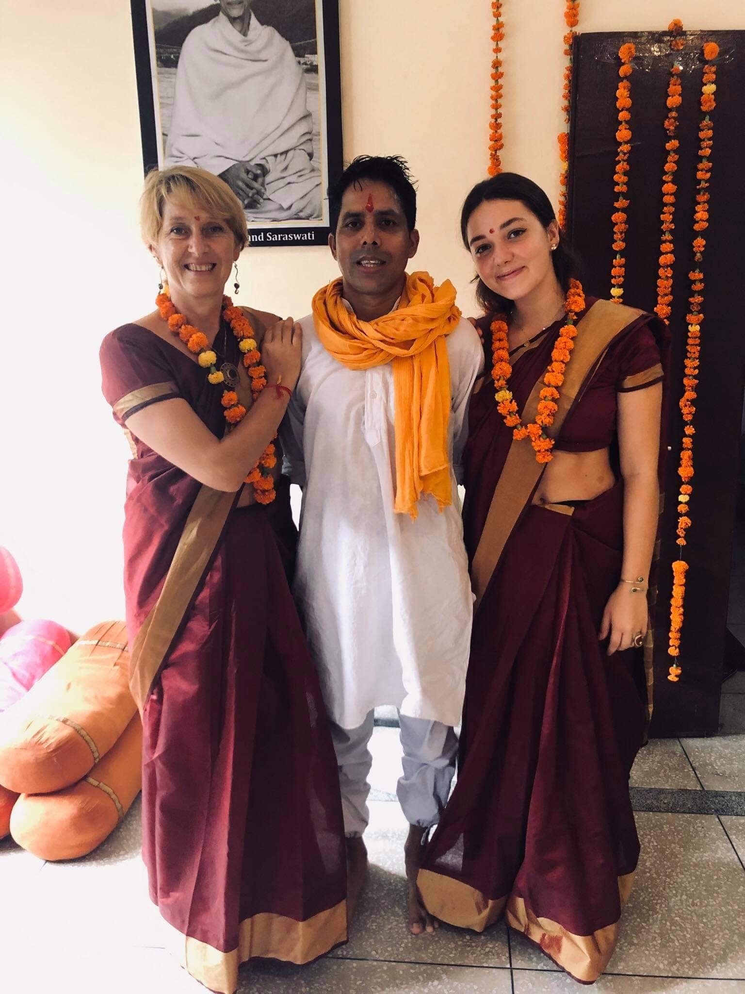 Véronique et Nell en saris bordeaux et guirlandes de fleurs orange, entourant leur professeur de yoga en Inde