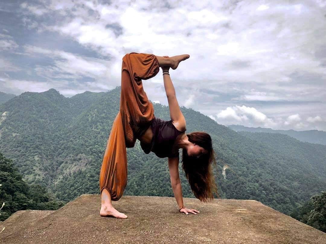 Posture de yoga en équilibre sur les mains, une jambe vers le ciel, sur un rocher face aux montagnes de l’Himalaya